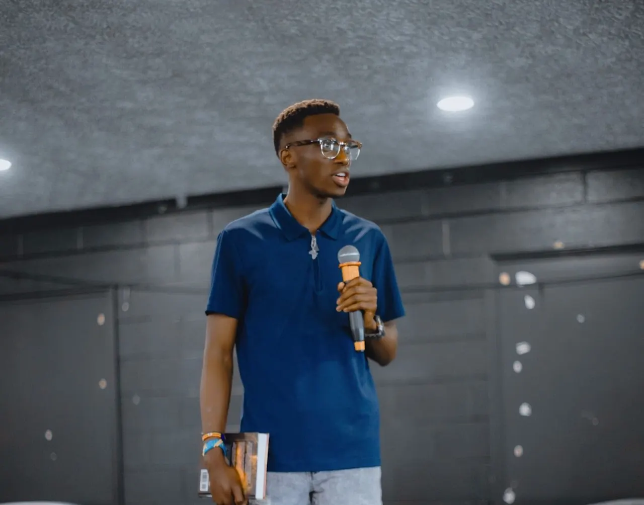 Fiston speaking on stage with a microphone.