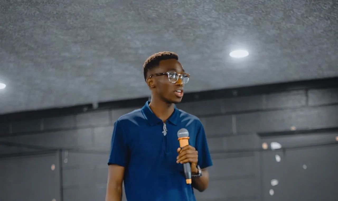 Fiston speaking to an audience with a microphone.