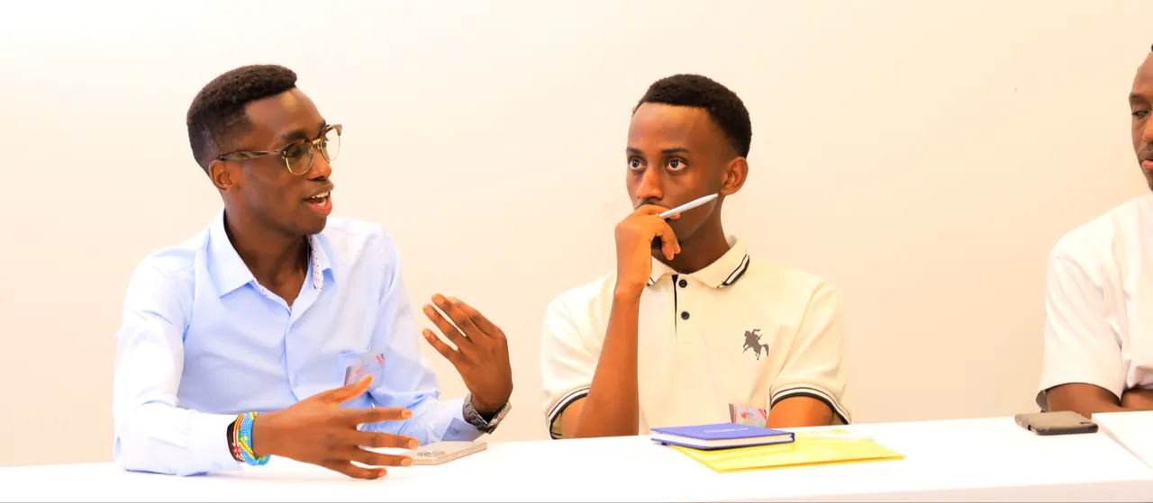 Fiston in conversation with a young man at a table.